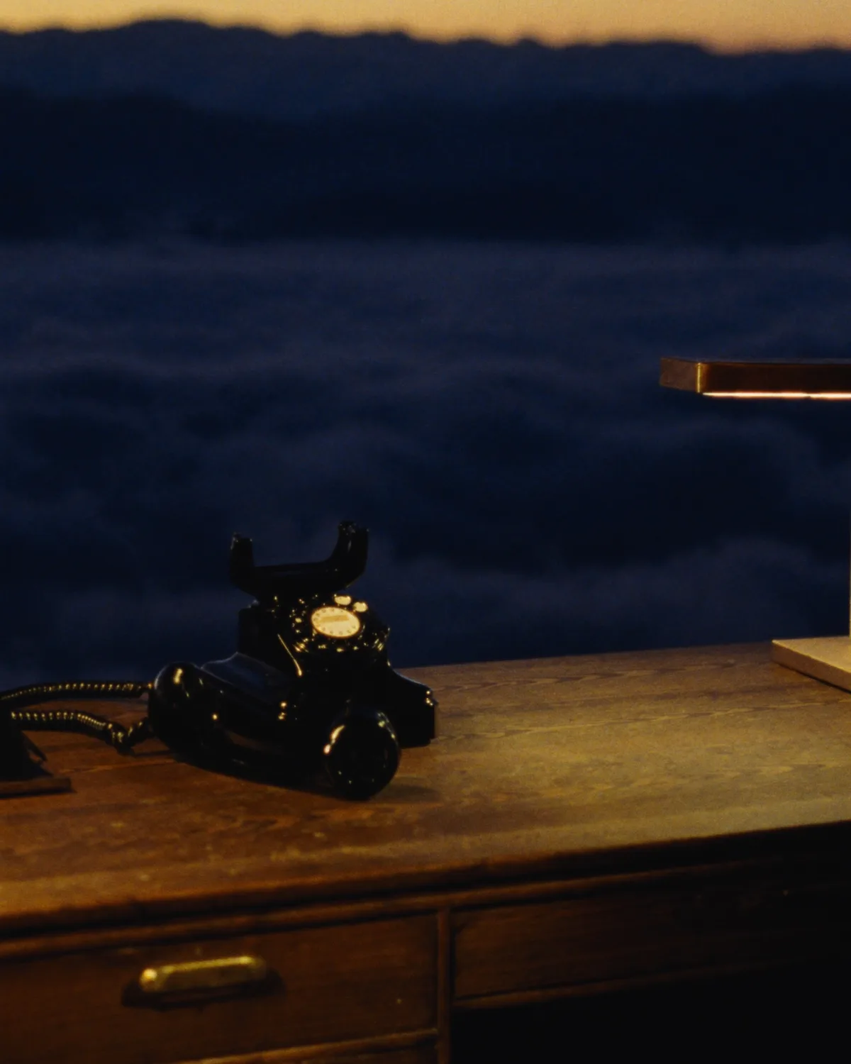 A black desk phone on a walnut desk at a mountain summit at dusk