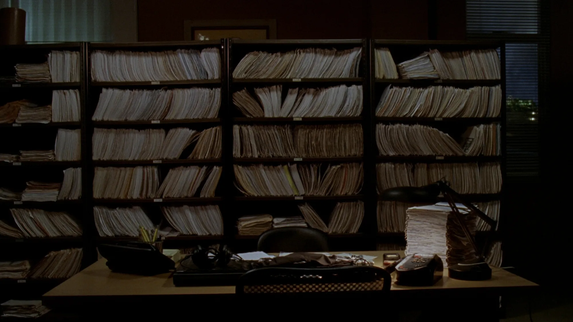 A law office after hours, shelves of case files and a desk phone under a lamp